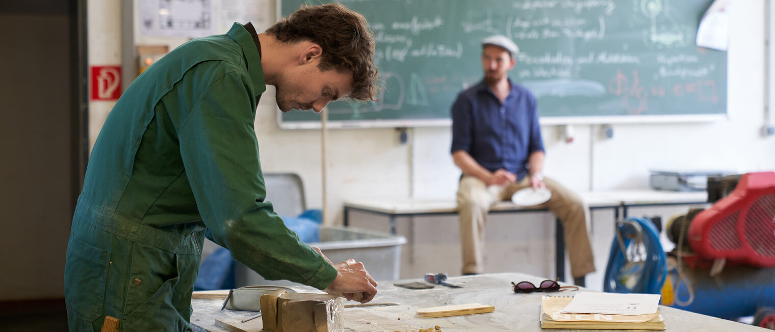 Student an der Akademie für Handwerksdesign Gut Rosenberg erstellt erste Entwurfe während der Dozent weitere Themen erklärt.