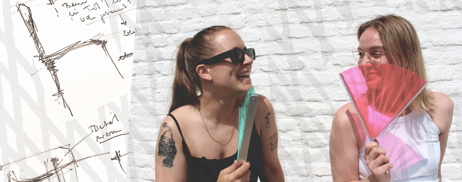 Zwei junge fröhliche Frauen sitzen in der Sonne mit einem Wind-Fächer in der Hand